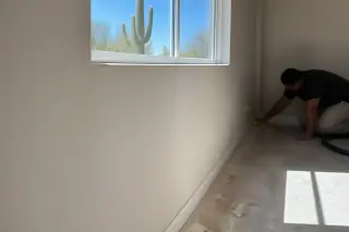 Worker cleaning baseboards below a smooth, sanded drywall patch in a Phoenix, AZ home.