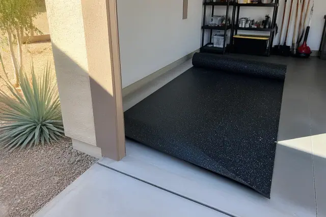 Worker unrolling recycled rubber flooring on a garage concrete floor in Mesa, AZ.