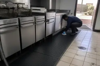 Worker wiping rubber mat edges in a Phoenix, AZ commercial kitchen with desert views through the door.
