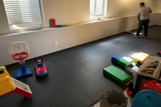 Technician sweeping rubber floor tiles in a Phoenix, AZ basement playroom with toys nearby.
