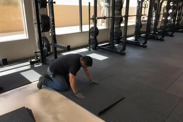 Technician installing heavy-duty rubber gym flooring onto a concrete slab in Phoenix, AZ.