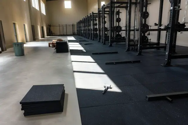 Technician installing heavy-duty rubber gym flooring onto a concrete slab in a Phoenix, AZ gym.