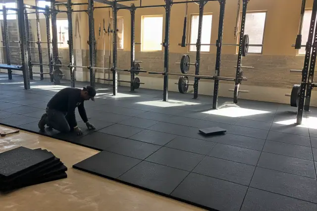 Technician installing rubber flooring tiles in a fitness center weight room in Gilbert, AZ.