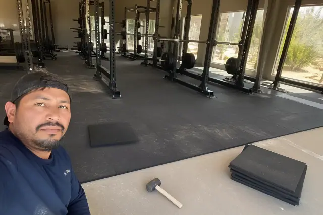 A technician installing rubber floor tiles in a Glendale, AZ fitness center free-weight zone.