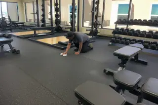 Technician wiping a seam on high-density rubber flooring in a Phoenix, AZ corporate gym.