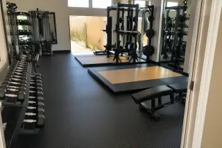 Rolled rubber flooring beneath weight racks in a Phoenix, AZ corporate gym with sunlight through the windows.
