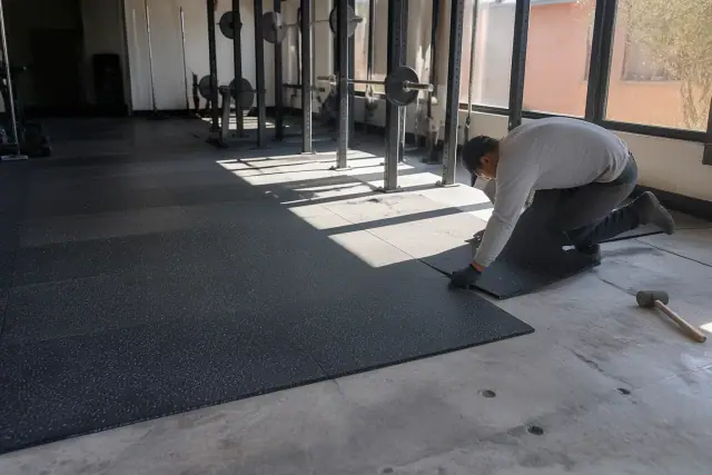 Technician installing heavy-duty rubber gym flooring on a concrete slab at a CrossFit facility in Phoenix, AZ.