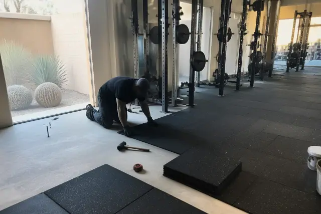 Technician installing rubber gym flooring in a weight room with desert views in Phoenix, AZ.