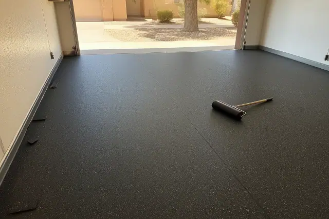 Black rubber flooring installed on a garage floor in Phoenix, AZ, with a hand roller nearby.