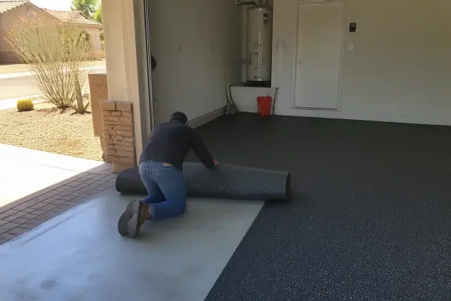 Worker installing rubber flooring on a concrete garage floor in a Chandler, AZ home.