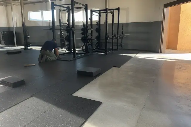Technician installing rubber gym flooring tiles on a concrete slab in a Phoenix, AZ fitness facility.