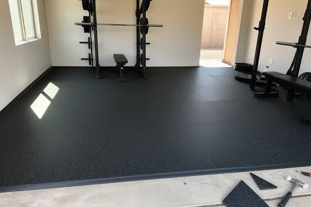 Technician installing rubber gym flooring on a concrete floor in a Glendale, AZ home gym.