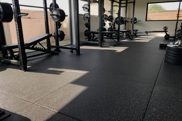 Technician installing heavy-duty rubber gym flooring on concrete in a Tempe, AZ training facility.