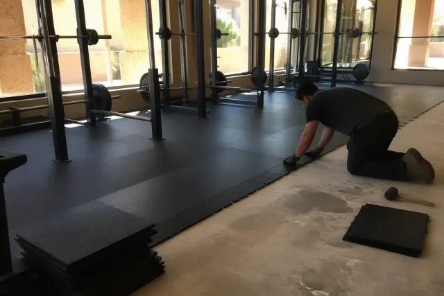 Technician installing rubber gym flooring tiles over concrete in a Phoenix, AZ facility.
