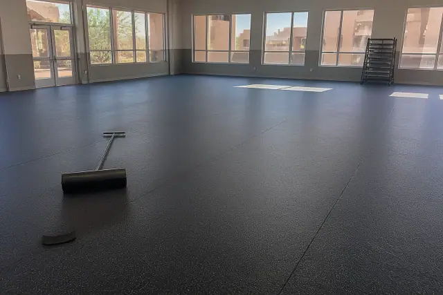 Newly installed rubber flooring in a school multipurpose room in Phoenix, AZ, showing seams and a floor roller.
