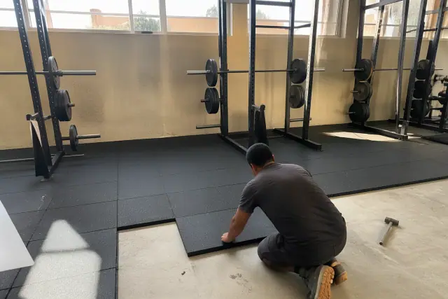 Technician installing high-density rubber gym flooring onto a concrete floor in Phoenix, AZ.