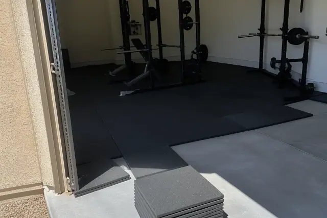 Technician installing black rubber gym flooring over a concrete slab in a Phoenix, AZ home gym.