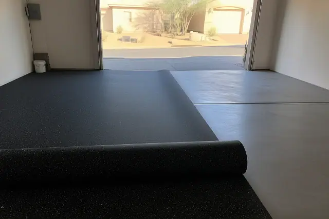 Worker unrolling industrial rubber flooring in a Phoenix, AZ garage with desert landscaping visible outside.