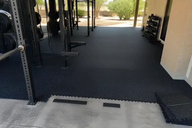 Technician installing heavy-duty rubber floor tiles in a gym with squat racks in Chandler, AZ.