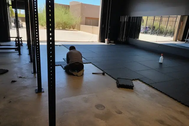 Technician installing heavy-duty interlocking rubber floor tiles at a fitness center in Phoenix, AZ.
