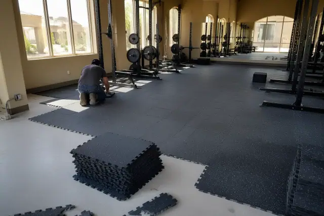 Technician installing heavy-duty rubber floor tiles in a Phoenix, AZ fitness center with squat racks.