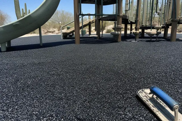 A technician trowels loose rubber mulch surfacing around play equipment at a park in Phoenix, AZ.