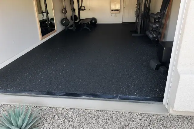 Rubber flooring installation in a Phoenix, AZ home garage with visible moisture barrier and desert landscaping outside.