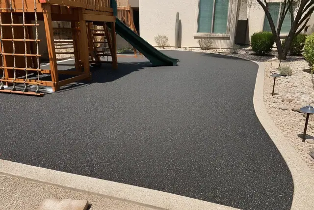 Technician troweling rubber flooring around play equipment in a Phoenix, AZ residential yard.