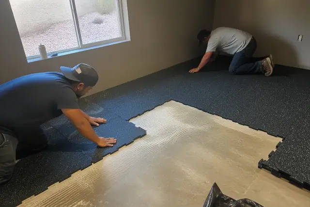 Contractors installing recycled rubber flooring on a concrete basement floor in Phoenix, AZ.