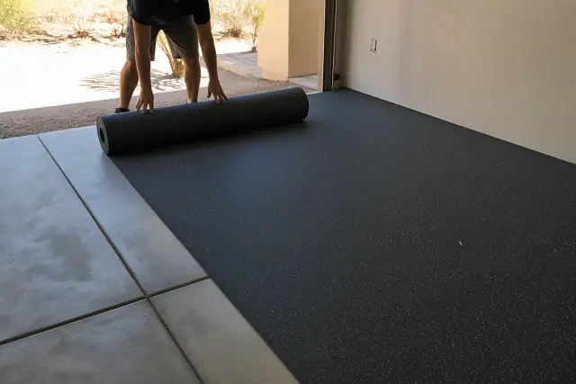 Worker unrolling recycled rubber flooring in a Phoenix, AZ garage workshop.