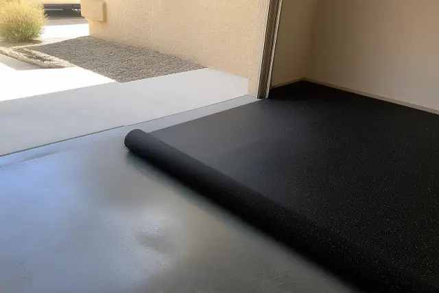 Worker installing rolled recycled rubber flooring on a concrete garage floor in Phoenix, AZ.