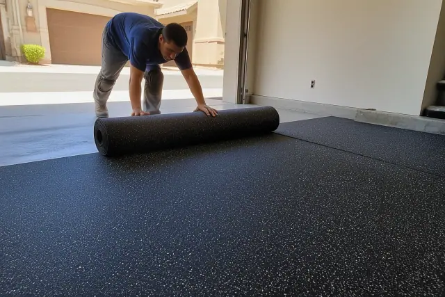 Worker unrolling recycled rubber flooring sheets on a garage concrete floor in Gilbert, AZ.