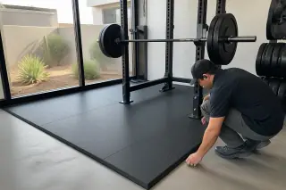Technician inspecting the seams of rolled rubber flooring under a squat rack at a gym in Phoenix, AZ.