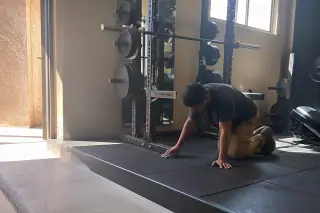 Technician cleaning rubber gym floor seams under a squat rack with desert sunlight visible in Phoenix, AZ.