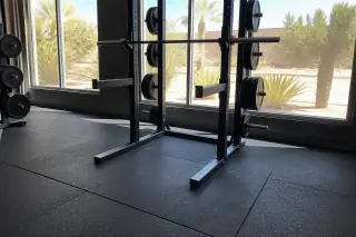 Thick rubber floor tiles installed under a squat rack in a Phoenix, AZ gym with desert views.