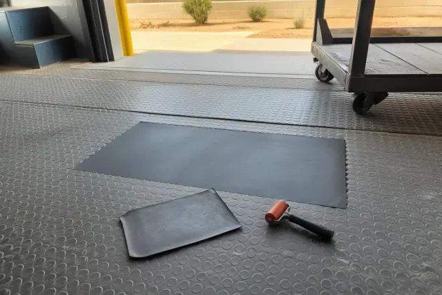 A flush rubber patch repair on warehouse loading dock flooring in Goodyear, AZ with a hand roller nearby.