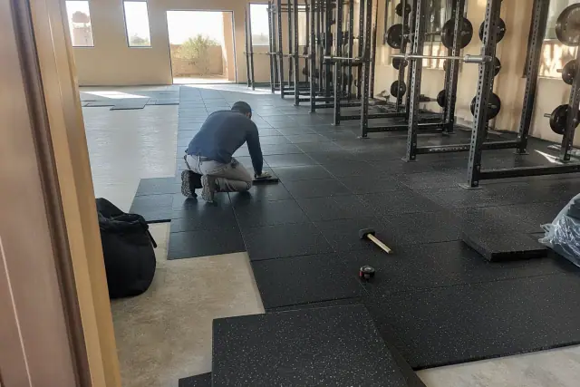 Technician installing heavy-duty rubber gym flooring on a concrete slab in Phoenix, AZ.