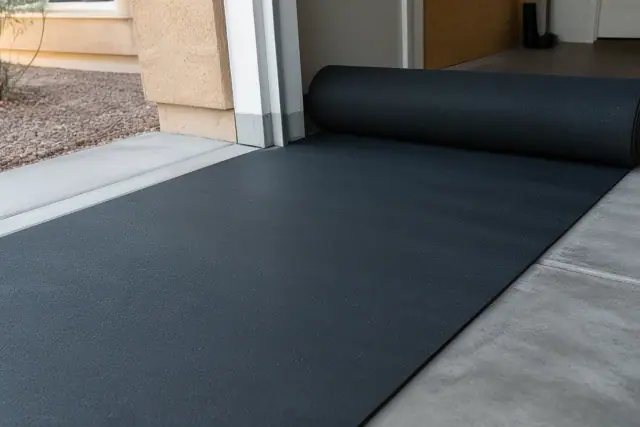 Worker unrolling sheets of recycled rubber flooring to create a sealed barrier on a garage floor in Phoenix, AZ.