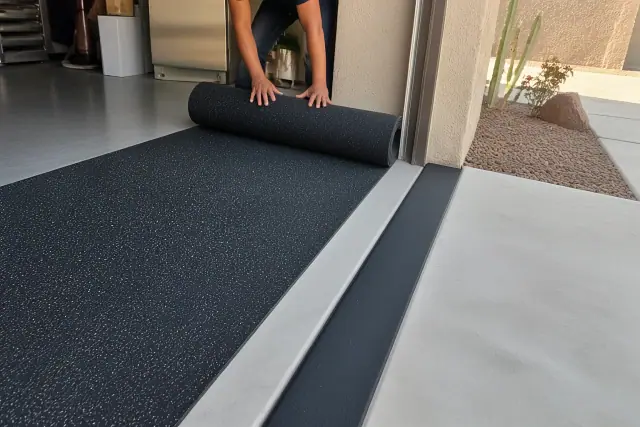 Worker installing recycled rubber flooring in a Phoenix, AZ garage with xeriscaping in the background.