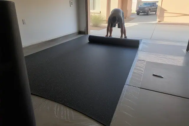 Worker installing sheets of recycled rubber flooring in a garage in Phoenix, AZ.
