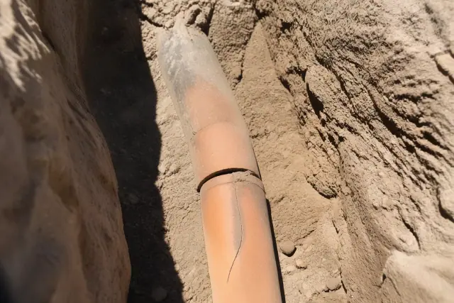 A cracked terra cotta pipe segment exposed in a deep trench with desert soil at a jobsite in Phoenix, AZ.