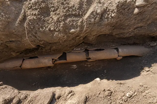 A segment of cracked terra cotta piping in a deep trench with compacted soil at an excavation site in Phoenix, AZ.