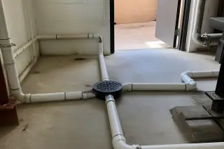 PVC drainage pipes and floor drain in an industrial utility room at a jobsite in Phoenix, AZ.