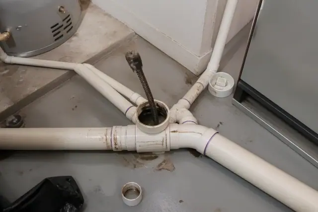 Drain snake cable and equipment cleaning a PVC floor drain junction in an industrial basement in Phoenix, AZ.