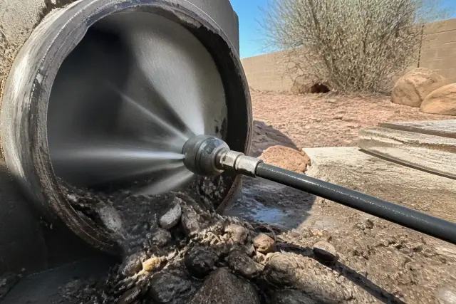 High-pressure hydro jetting nozzle clearing debris from a drain pipe at a work site in Phoenix, AZ.