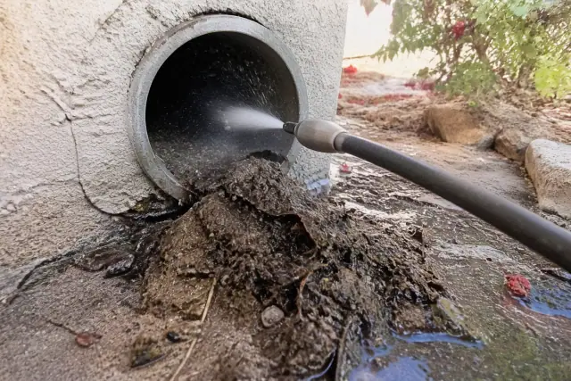 High-pressure hose clearing debris from a residential drainage pipe in Phoenix, AZ.