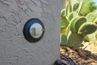 New metallic sewer cleanout plug installed in a stucco wall with cactus landscaping in Phoenix, AZ.