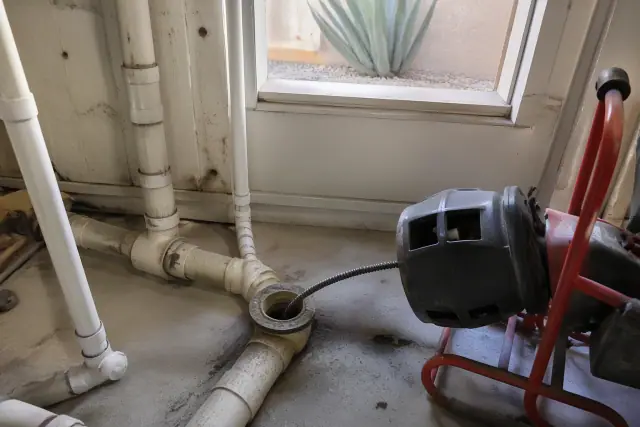 Mechanical rooter cable inserted into PVC drainage pipes in an industrial basement in Phoenix, AZ.