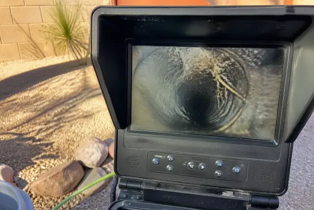 Portable sewer camera monitor displaying pipe walls and tree roots at a residential jobsite in Phoenix, AZ.