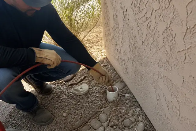 Technician feeding a sewer camera cable into a cleanout pipe at a job site in Scottsdale, AZ.